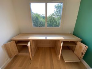 Télétravail sur un grand bureau et sa bibliothèque en bois naturel